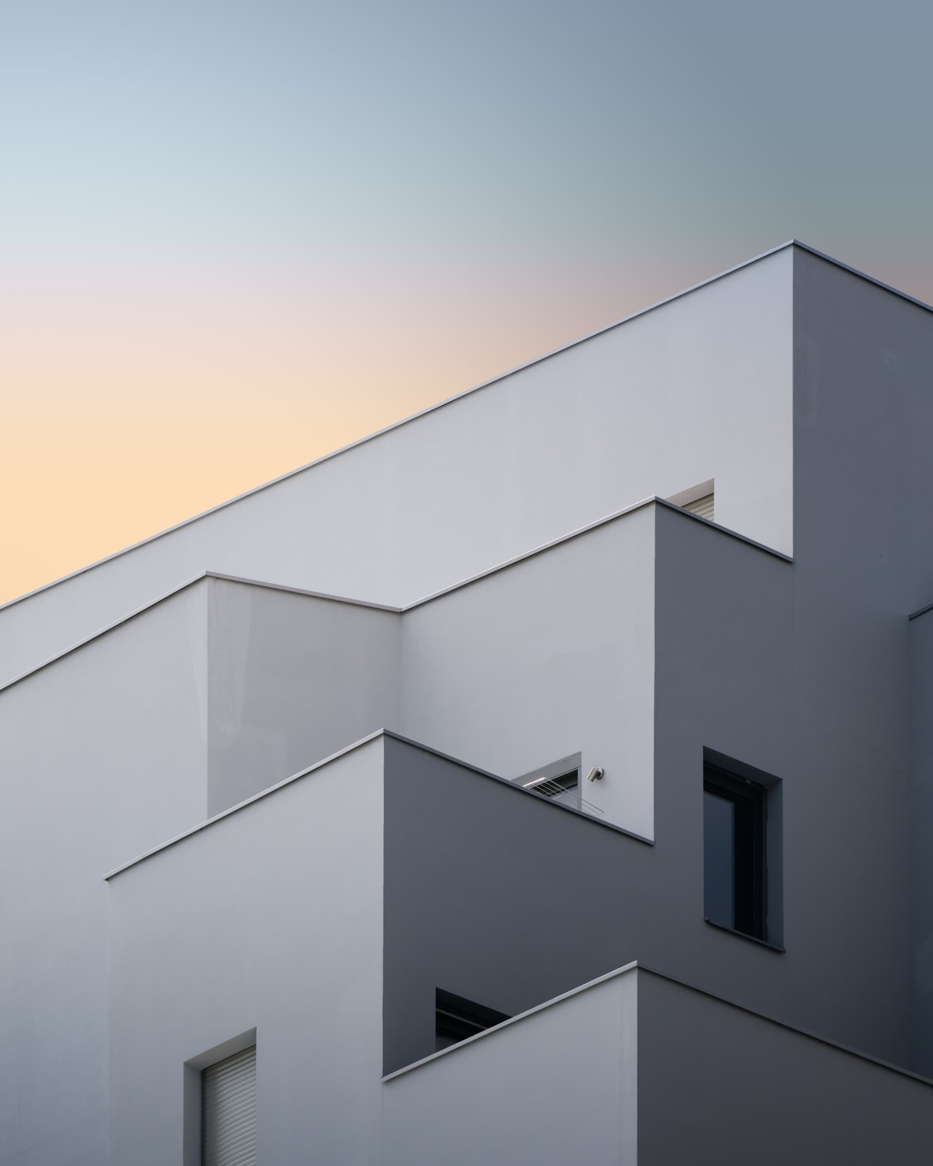 Modern light-gray building facade with staggered geometric volumes against a soft sky